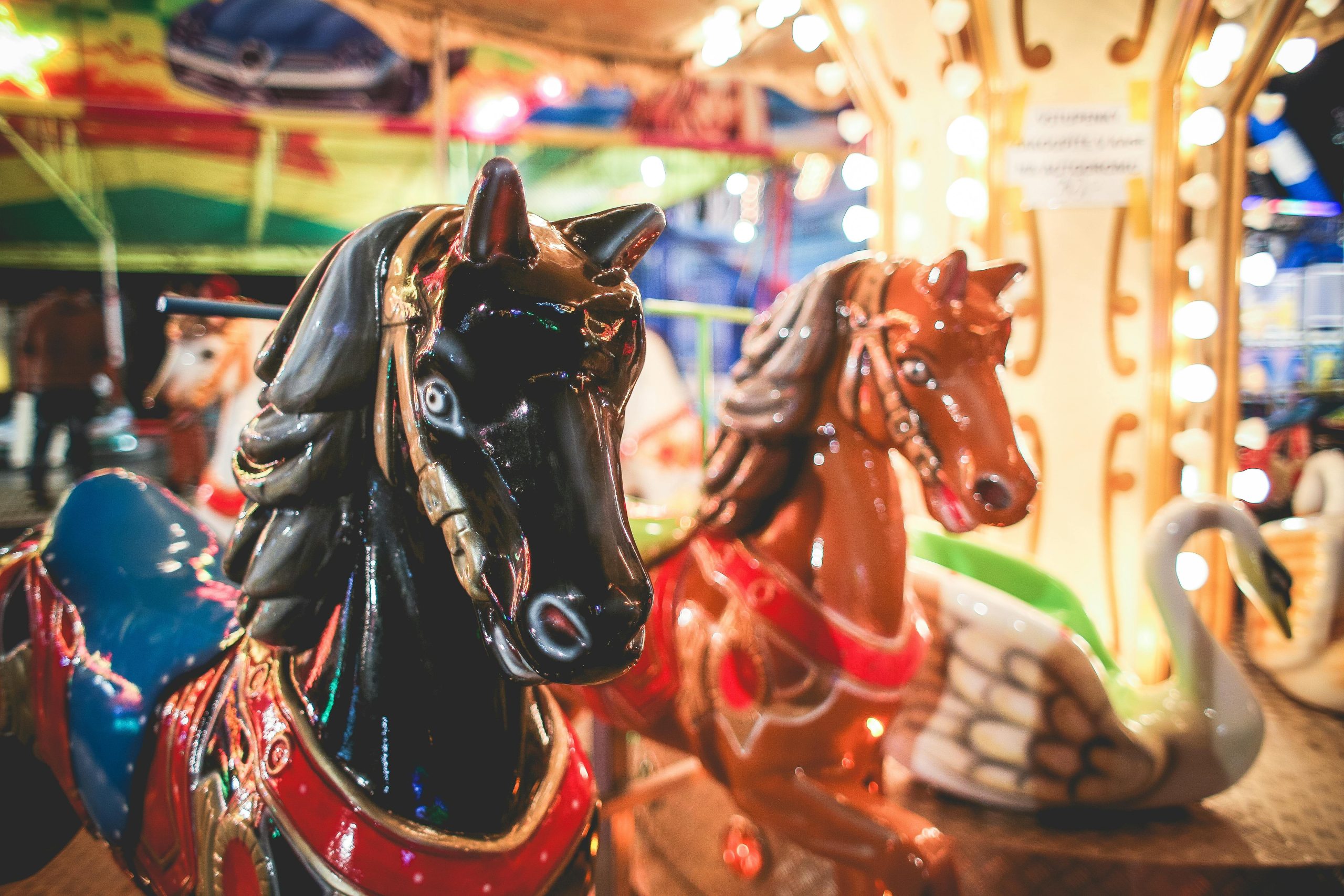 Brightly lit carousel horses at a festive night fairground with colorful lights.