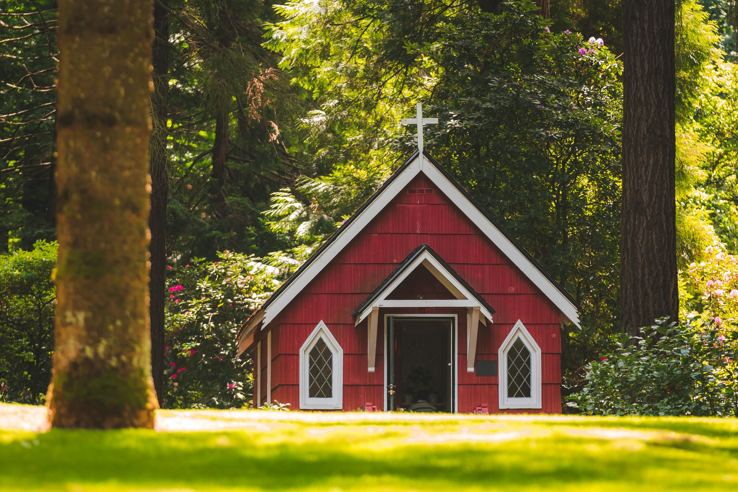 A small red chapel with a white cross nestled in a lush green forest in Portland, Oregon.