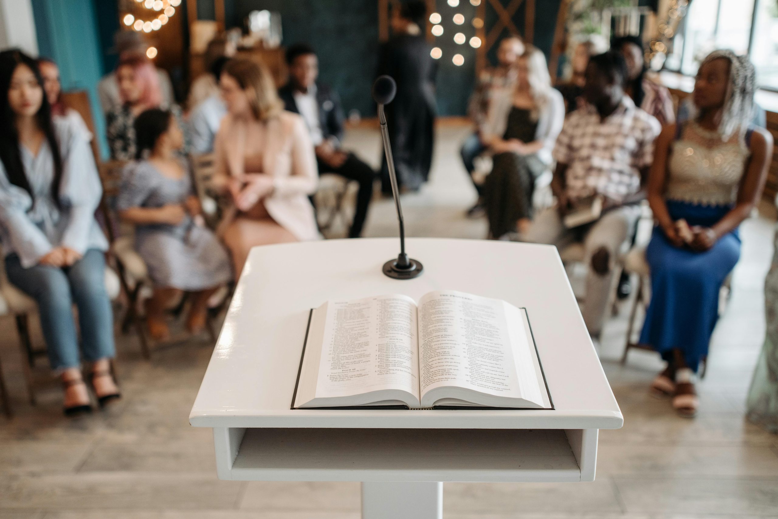 A microphone and open book on a podium in front of an audience in a church setting.